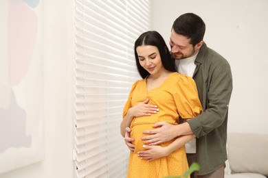 Pregnant woman with her husband indoors, space for text