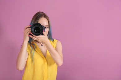 Young female photographer with camera on color background