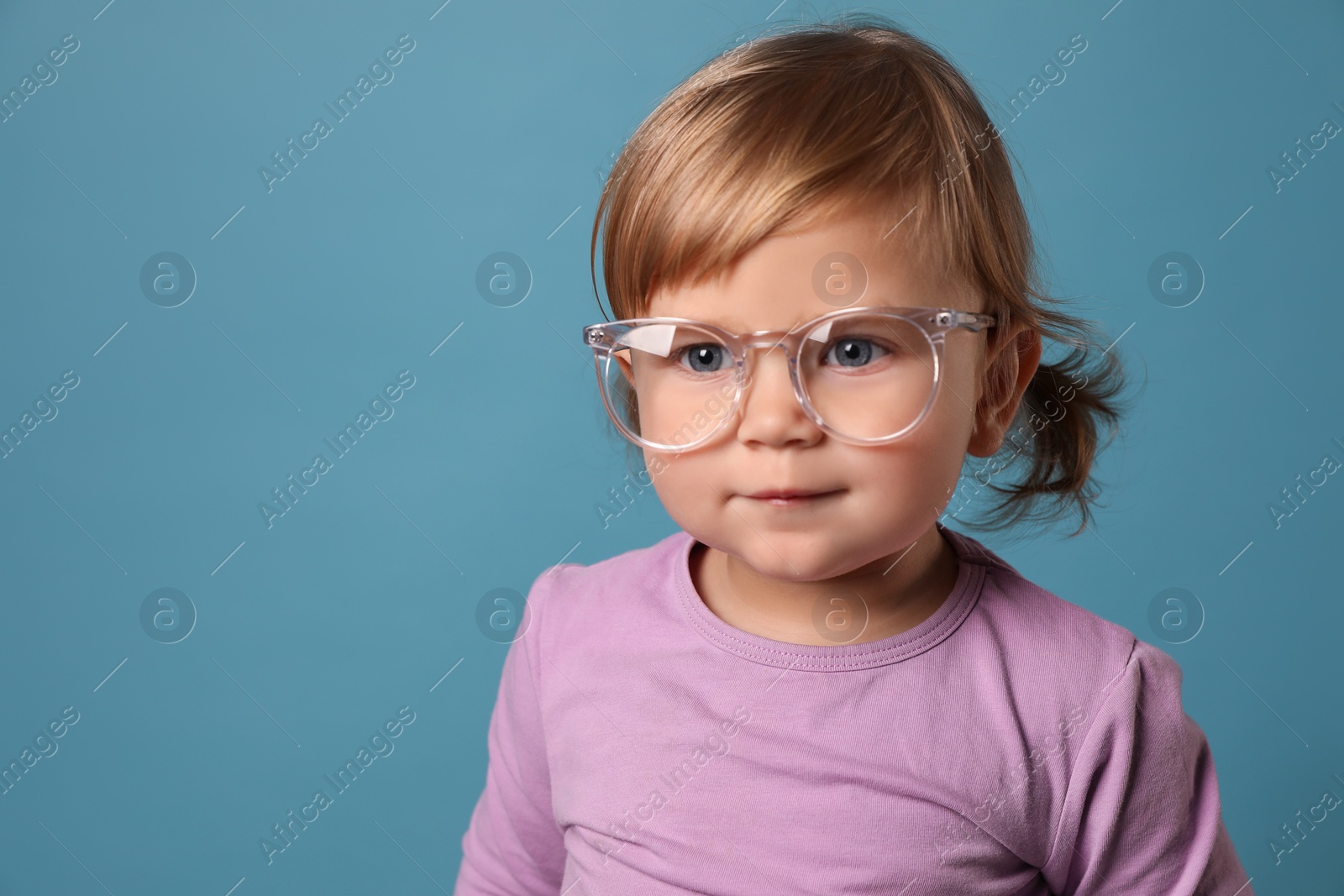 Photo of Cute little girl in glasses on light blue background. Space for text