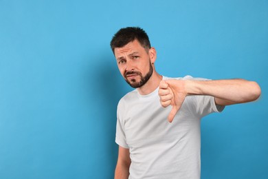 Photo of Man showing thumb down on light blue background, space for text