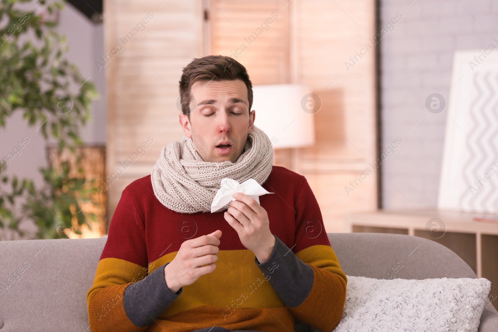 Photo of Sick young man with tissue suffering from cold on sofa at home