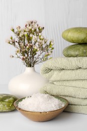 Photo of Composition with sea salt, spa stones, towels and flowers on white table against wooden background