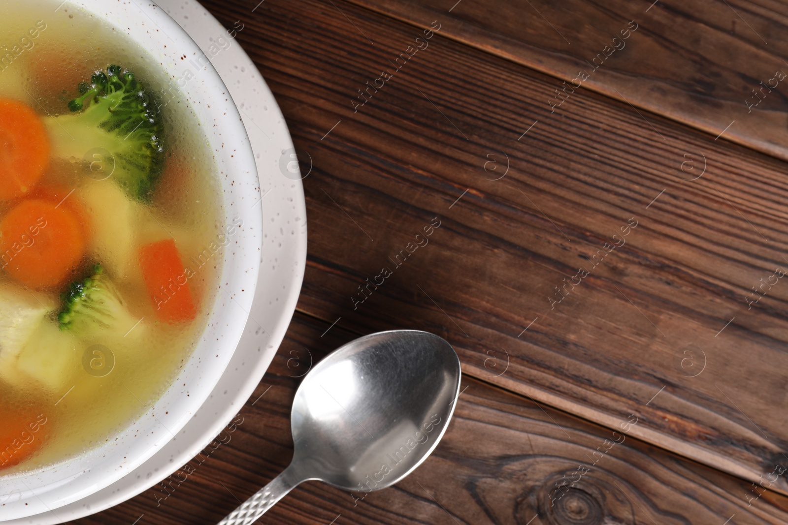 Photo of Tasty chicken soup with vegetables in bowl served on wooden table, top view. Space for text