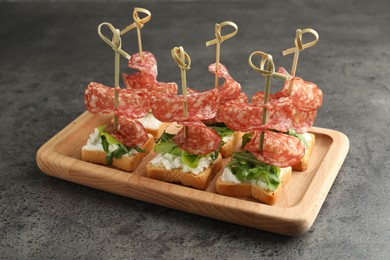 Photo of Tasty canapes with salami, greens and cream cheese on grey table