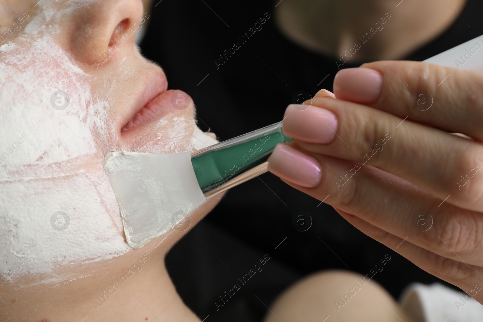 Photo of Cosmetologist applying mask on woman's face, closeup