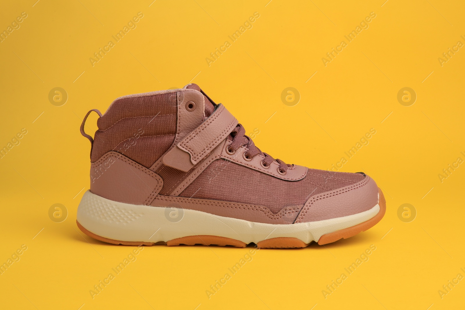 Photo of Stylish pink kid's sneaker on yellow background