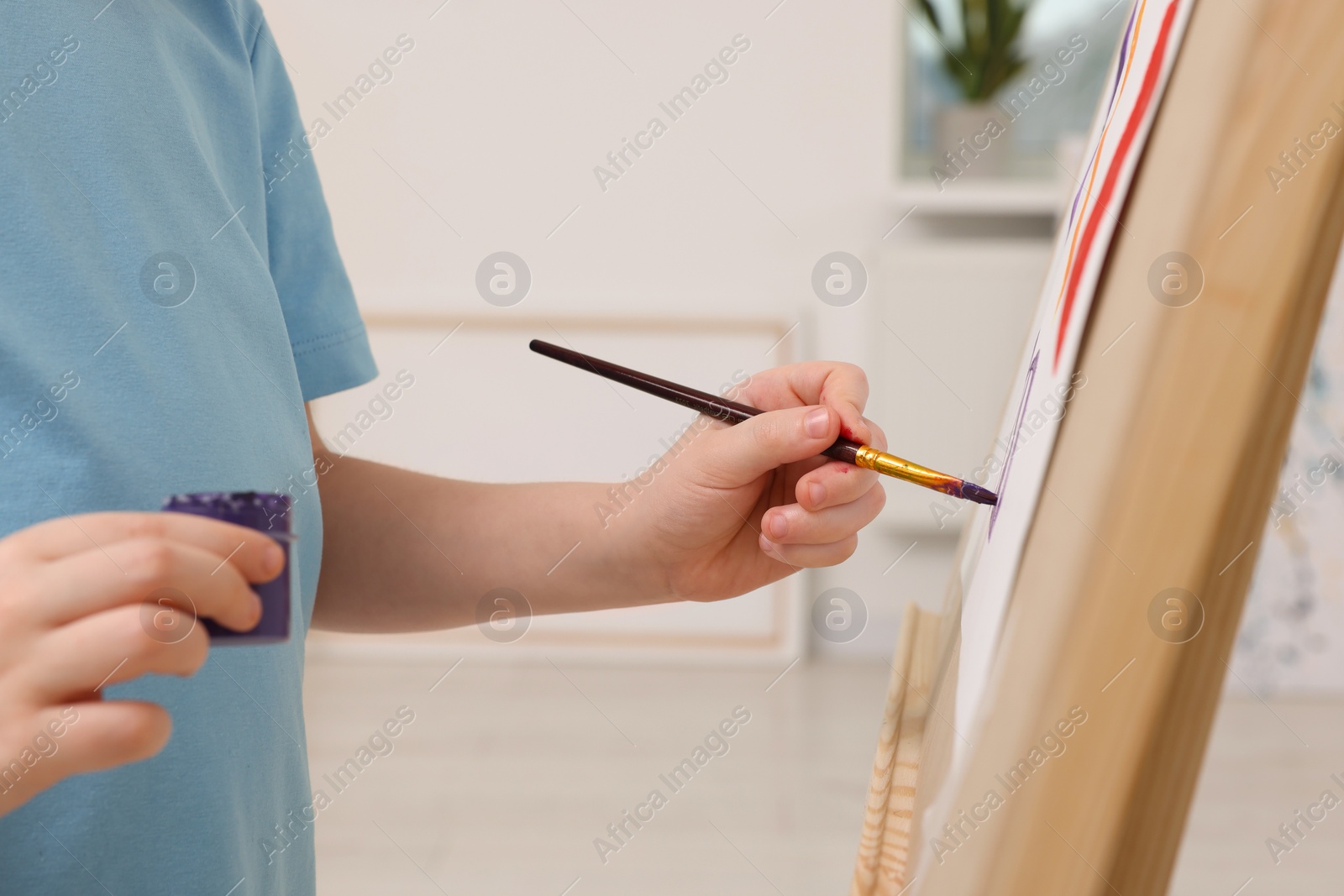 Photo of Little boy painting in studio, closeup. Using easel to hold canvas