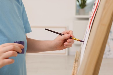 Little boy painting in studio, closeup. Using easel to hold canvas