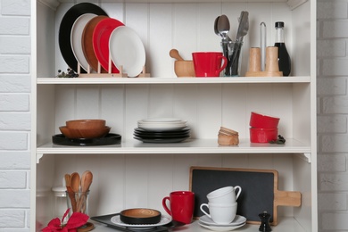 Photo of White shelving unit with set of dishware near brick wall