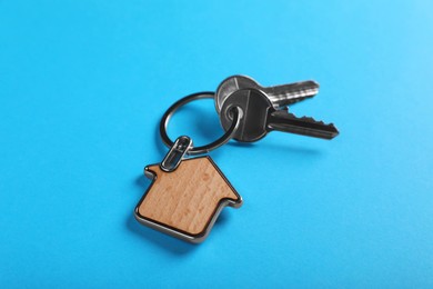 Photo of Keys with trinket in shape of house on blue background, closeup. Real estate agent services