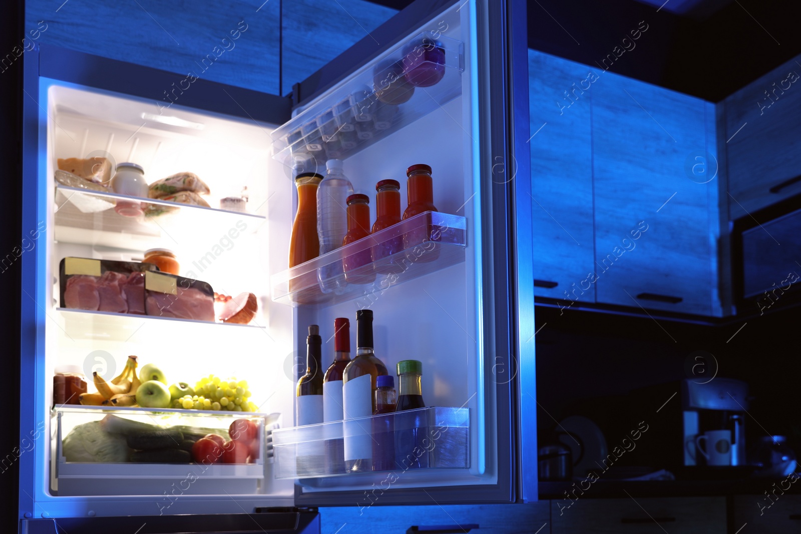 Photo of Open refrigerator full of products in kitchen at night