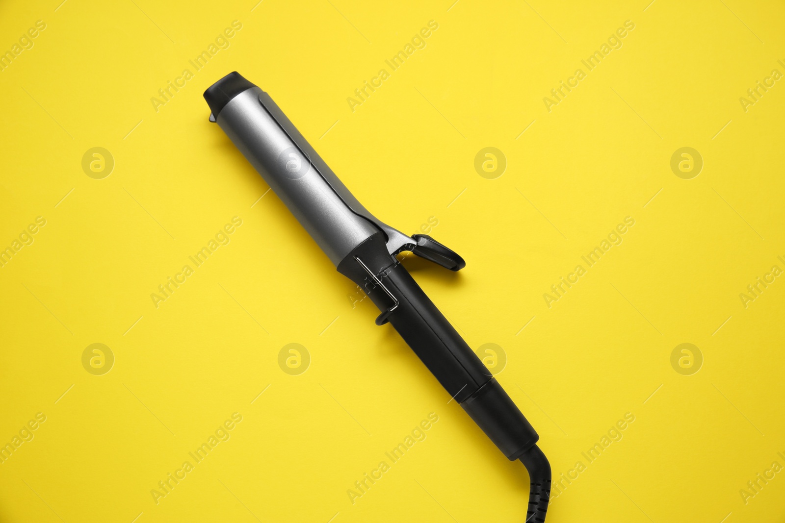 Photo of Hair curling iron on yellow background, top view