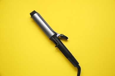 Photo of Hair curling iron on yellow background, top view
