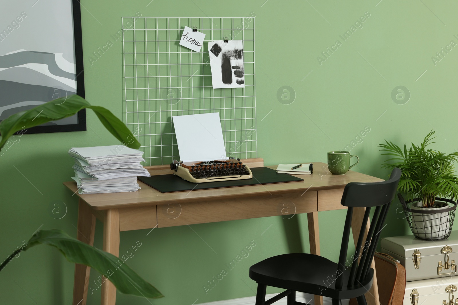 Photo of Typewriter, stack of papers and mood board on wooden table near pale green wall. Writer's workplace