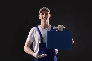 Professional repairman with tool box on black background