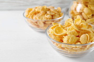 Photo of Glass bowl of tasty crispy corn flakes on white wooden table, space for text