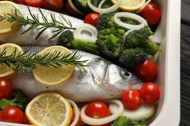 Photo of Raw fish with vegetables and lemon in baking dish on table