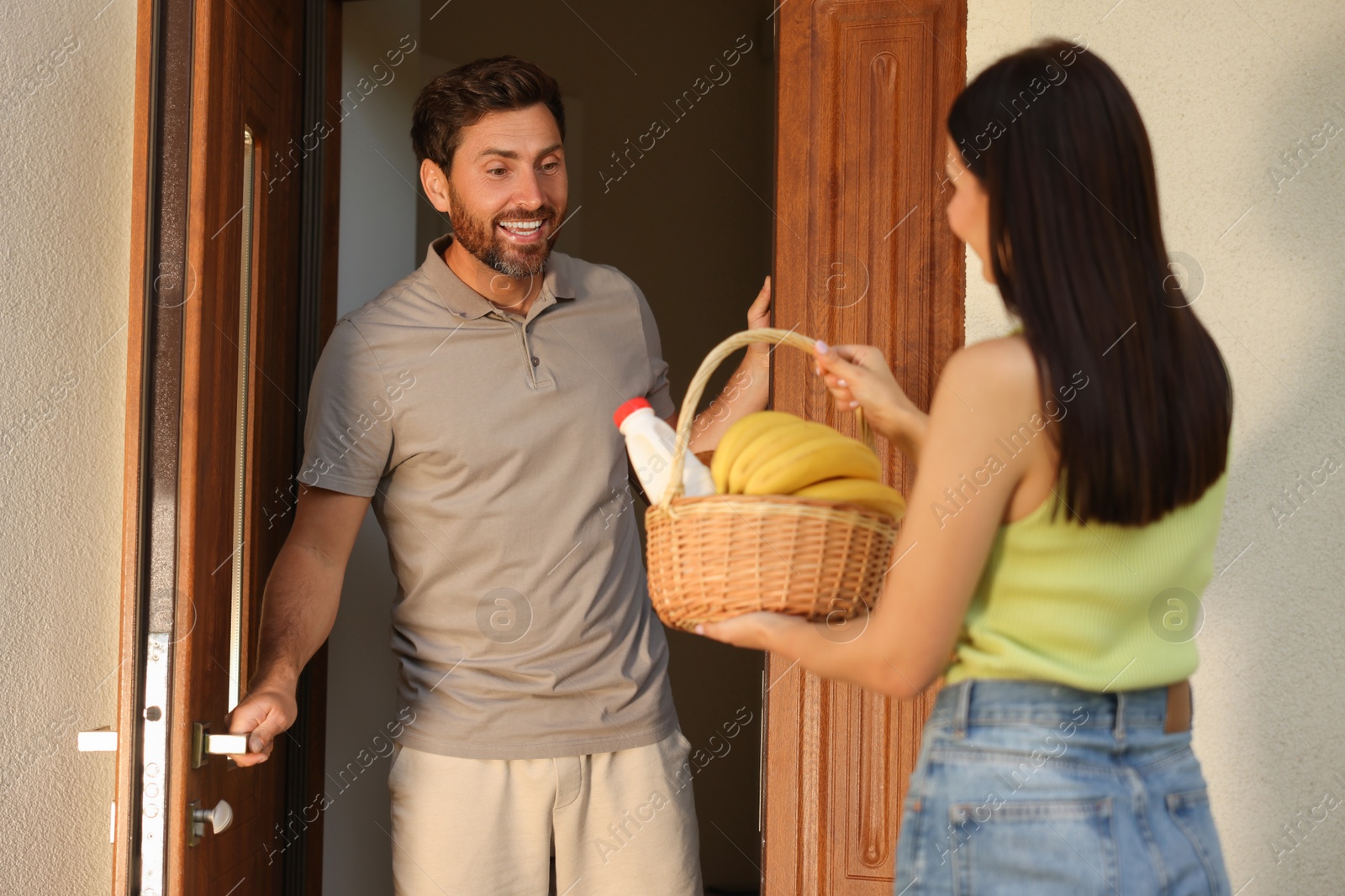 Photo of Friendly relationship with neighbours. Young woman with wicker basket of products treating man outdoors