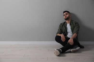 Sad man sitting on floor near light grey wall. Space for text