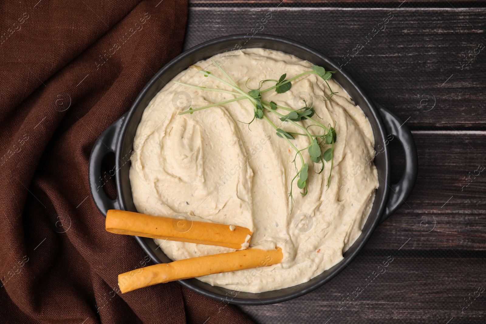 Photo of Delicious hummus with grissini sticks on wooden table, top view