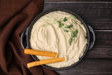 Photo of Delicious hummus with grissini sticks on wooden table, top view