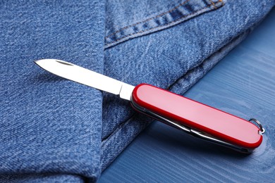 Photo of Modern compact portable multitool and jeans on blue wooden table