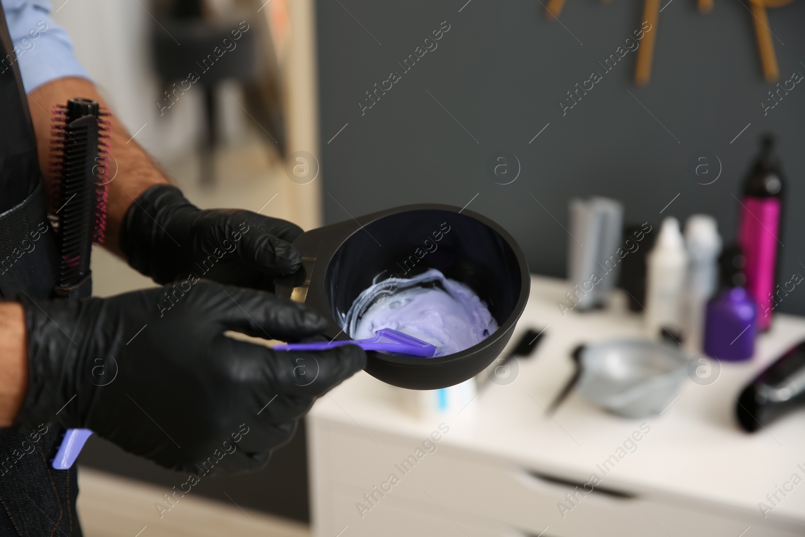 Photo of Professional hairdresser holding bowl with hair dye in beauty salon, closeup