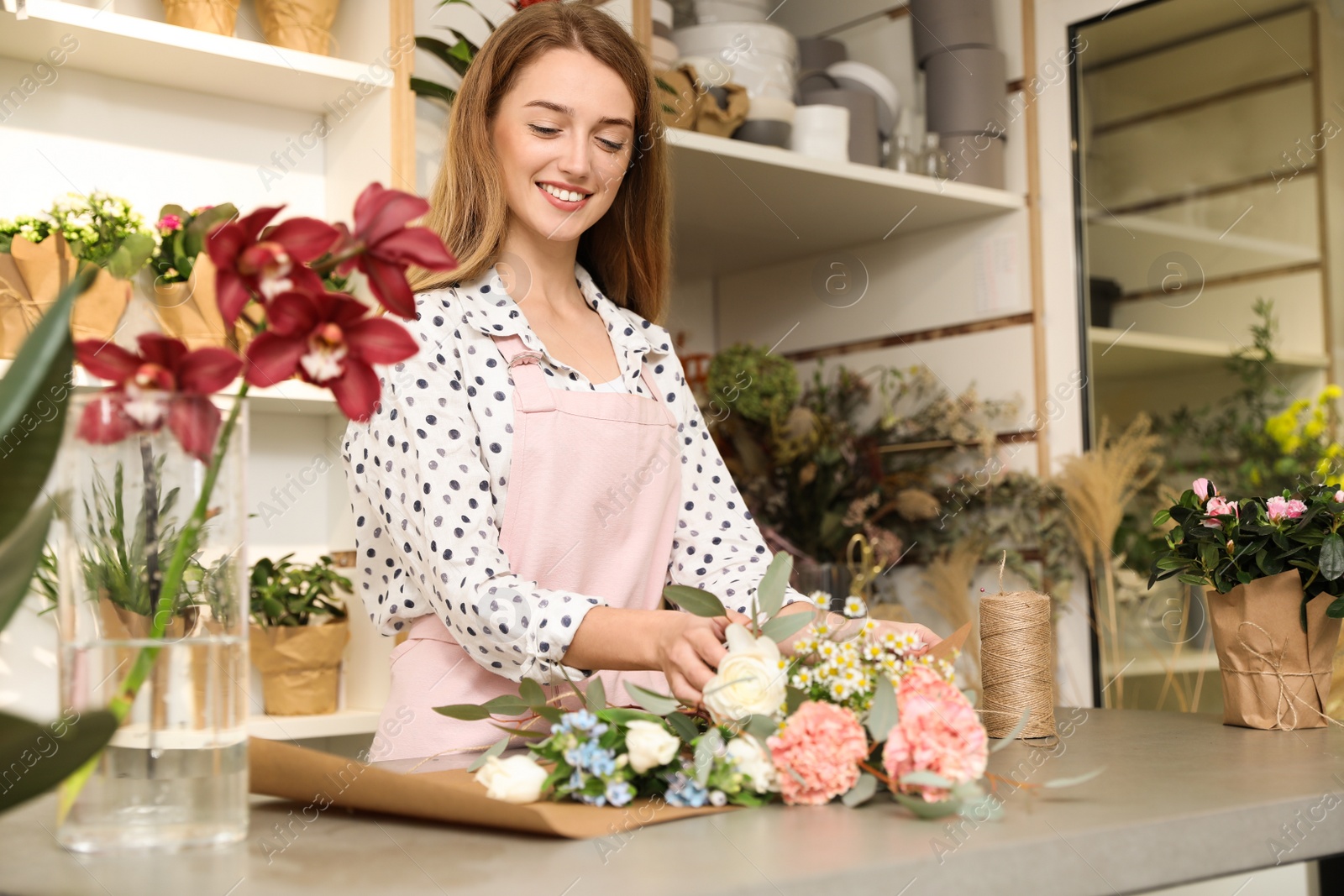 Photo of Florist making bouquet with fresh flowers at table in shop