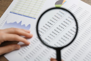 Photo of Woman looking at accounting document through magnifying glass at table, closeup