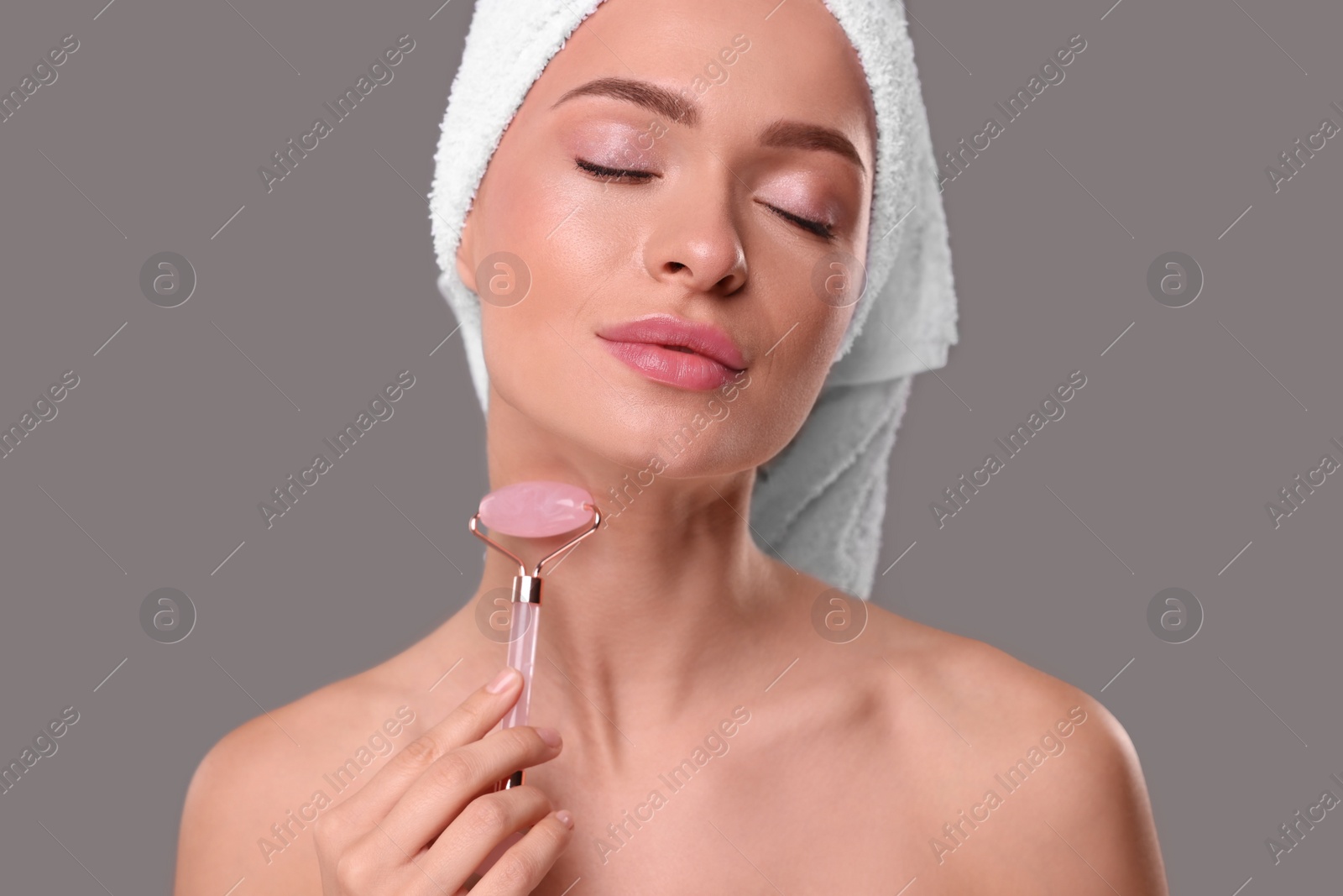 Photo of Young woman massaging her face with rose quartz roller on grey background