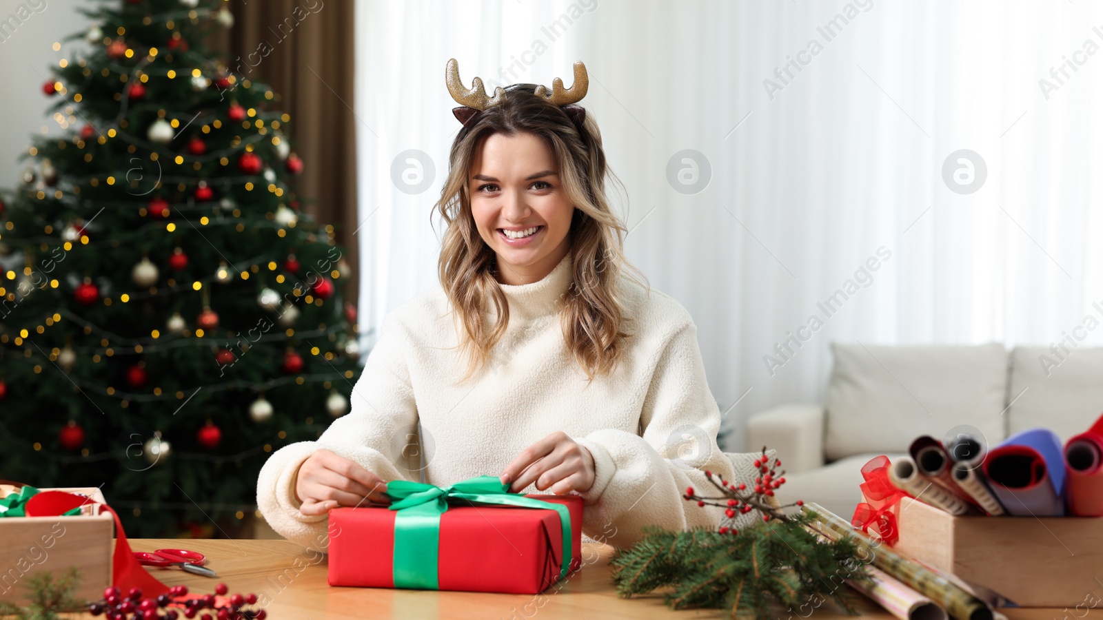 Photo of Beautiful young woman wrapping Christmas gift at home