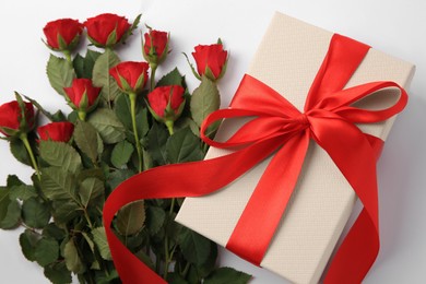 Photo of Beautiful gift box with bow and red roses on white background, top view
