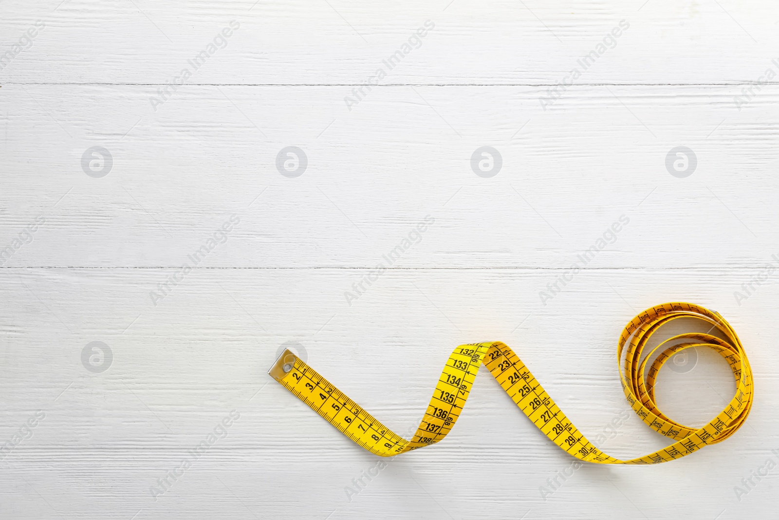 Photo of Yellow measuring tape on white wooden table, top view. Space for text