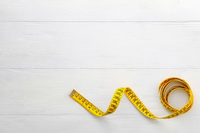 Photo of Yellow measuring tape on white wooden table, top view. Space for text