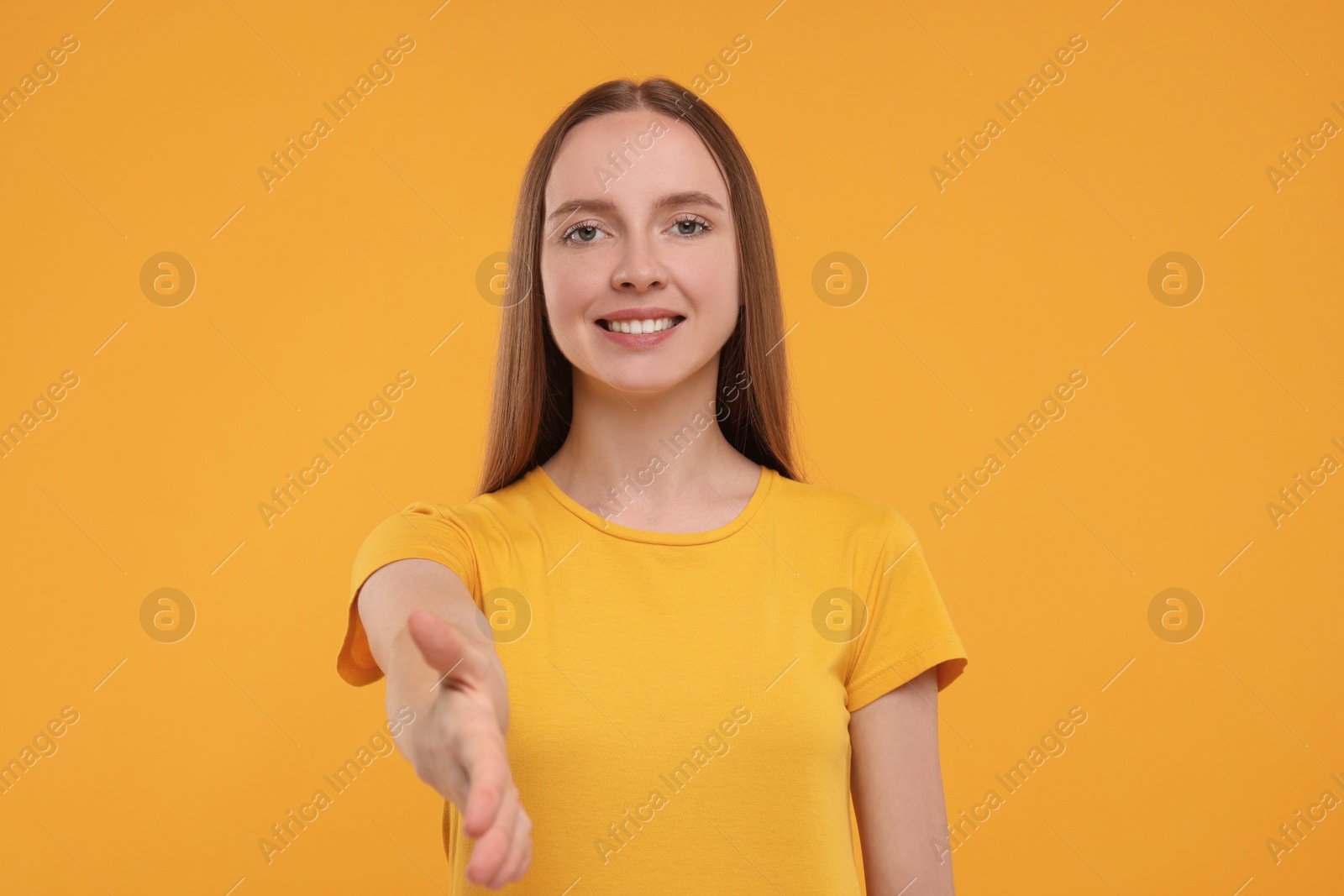 Photo of Happy young woman welcoming and offering handshake on yellow background