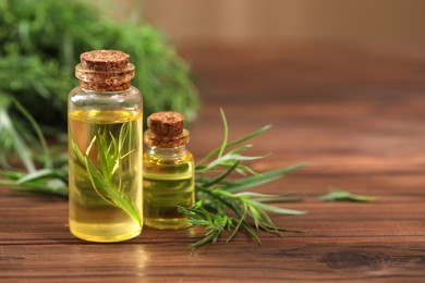 Bottles of essential oil and fresh tarragon leaves on wooden table. Space for text