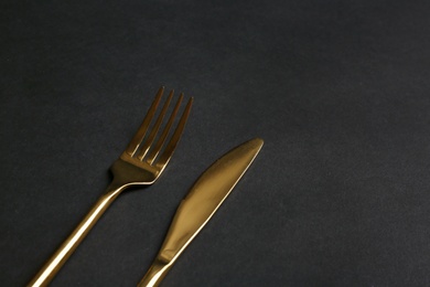 Photo of Gold fork and knife on black background. Space for text