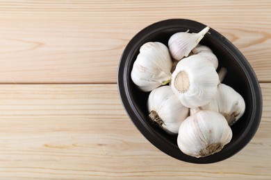 Fresh garlic bulbs in bowl on wooden table, top view. Space for text