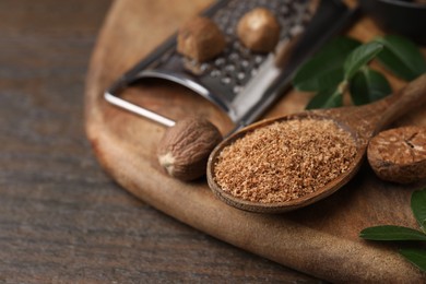 Spoon with grated nutmeg and green leaves on wooden table, closeup. Space for text