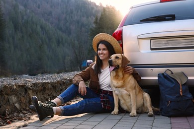 Happy woman and adorable dog sitting near car in mountains. Traveling with pet