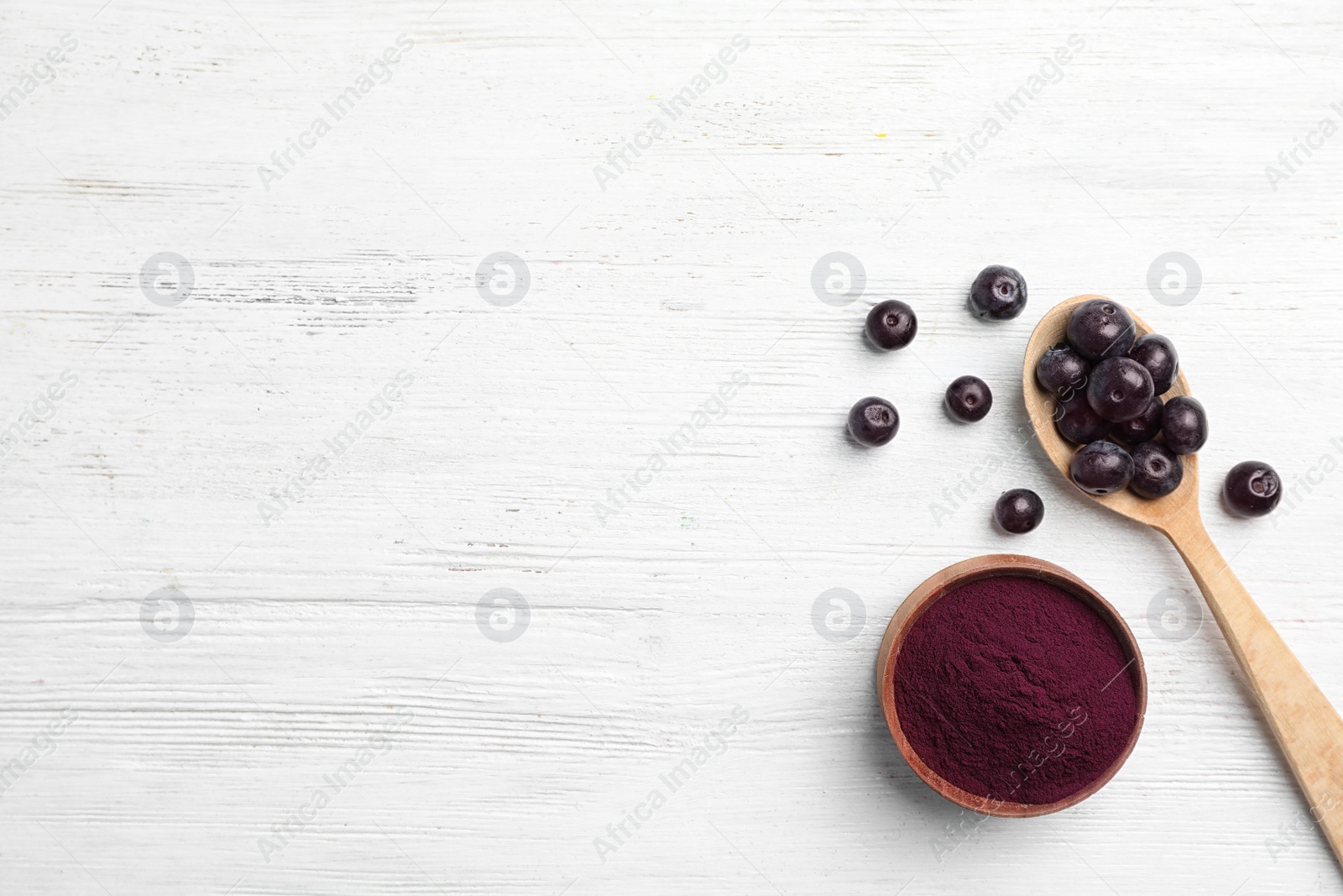 Photo of Bowl of acai powder and fresh berries on light wooden table, flat lay with space for text