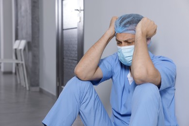 Exhausted doctor near grey wall in hospital, space for text