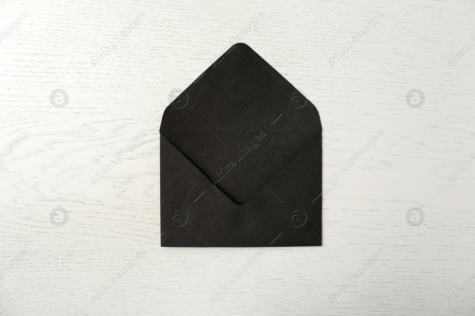 Photo of Black paper envelope on white wooden background, top view