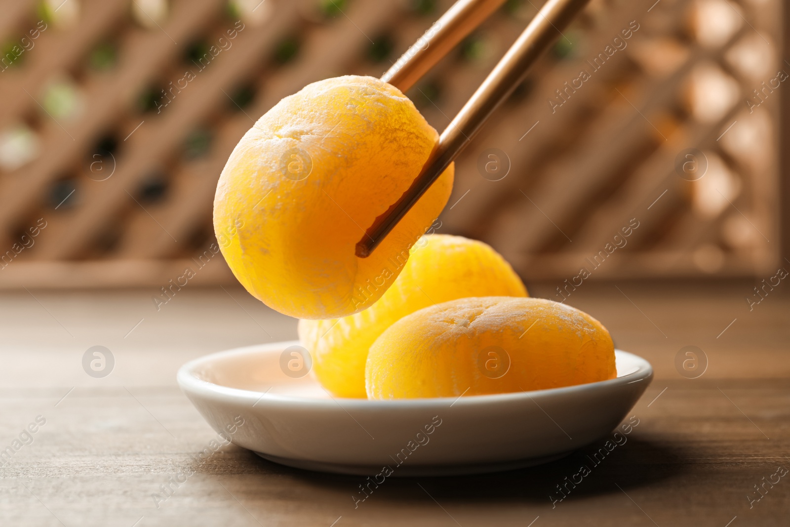 Photo of Taking delicious mochi from plate with chopsticks on wooden table. Traditional Japanese dessert