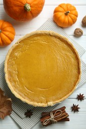 Delicious pumpkin pie and ingredients on white wooden table, flat lay