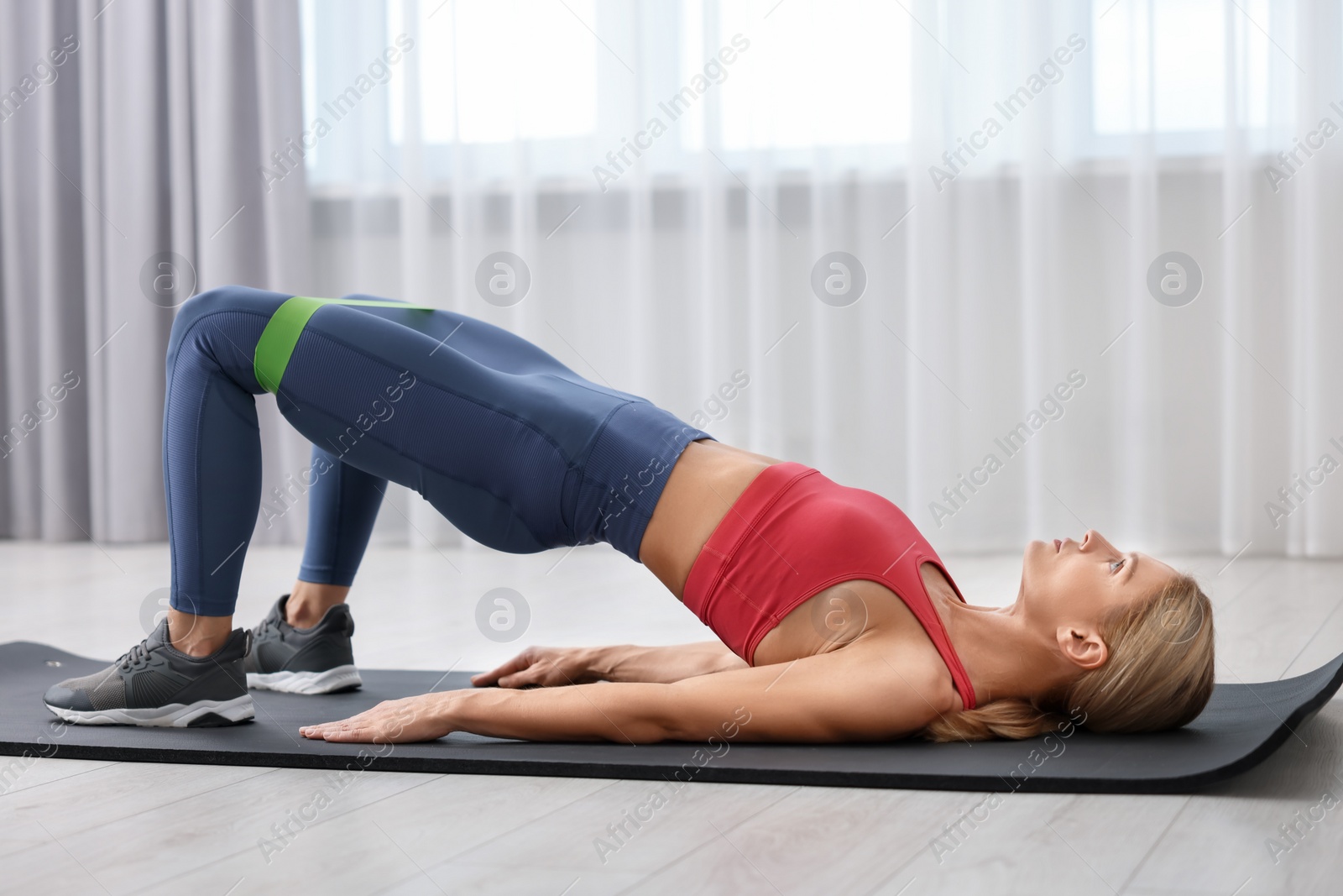 Photo of Athletic woman doing exercise with fitness elastic band on mat indoors