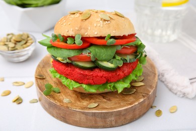 Photo of Tasty vegan burger with vegetables, patty and microgreens on white tiled table, closeup