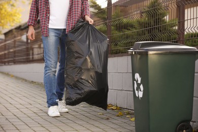 Photo of Man carrying garbage bag to recycling bin outdoors, closeup