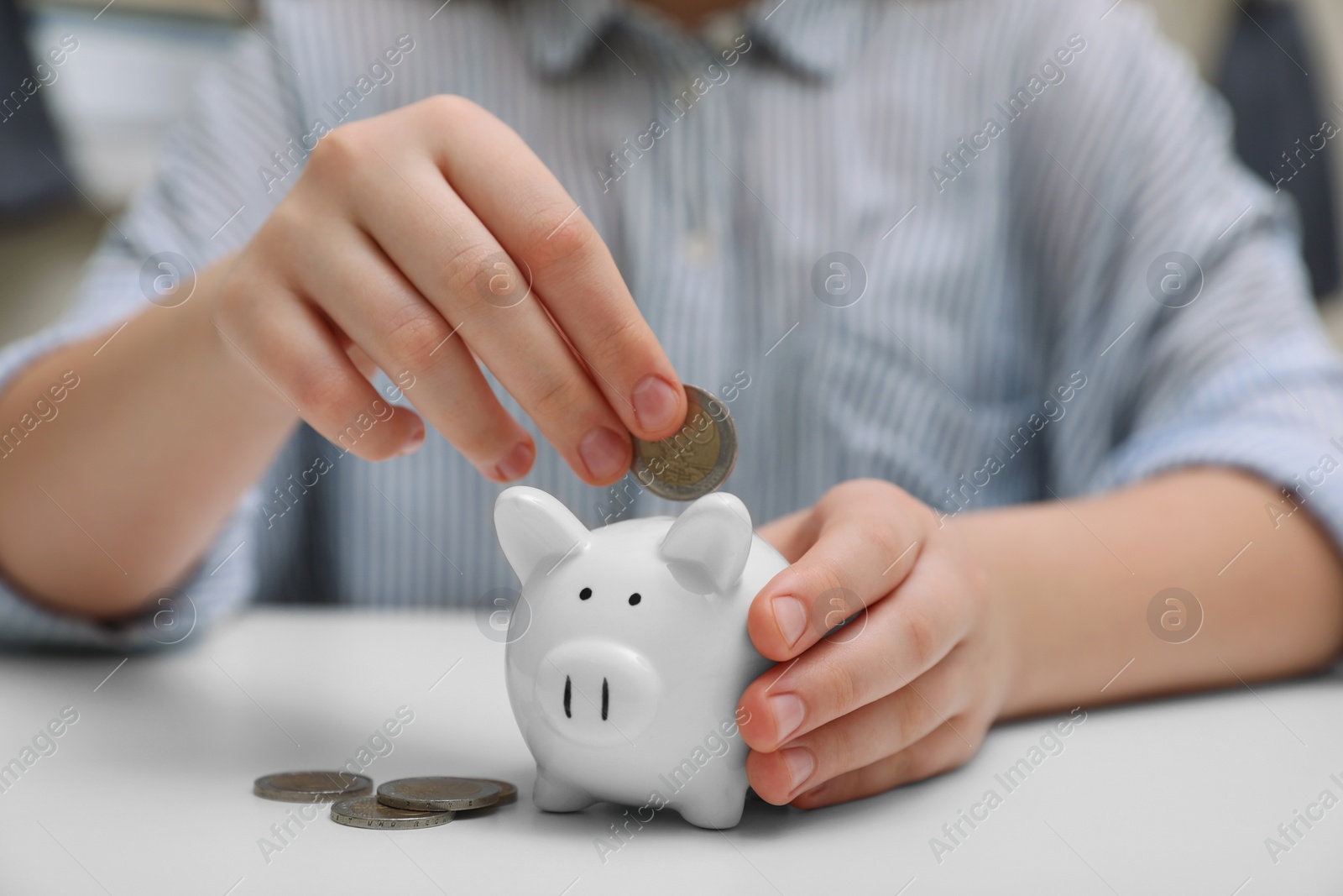 Photo of Woman putting coin into ceramic piggy bank at white wooden table, closeup. Financial savings