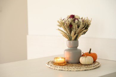 Photo of Beautiful bouquet of dry flowers, small pumpkins and candle on white table indoors, space for text